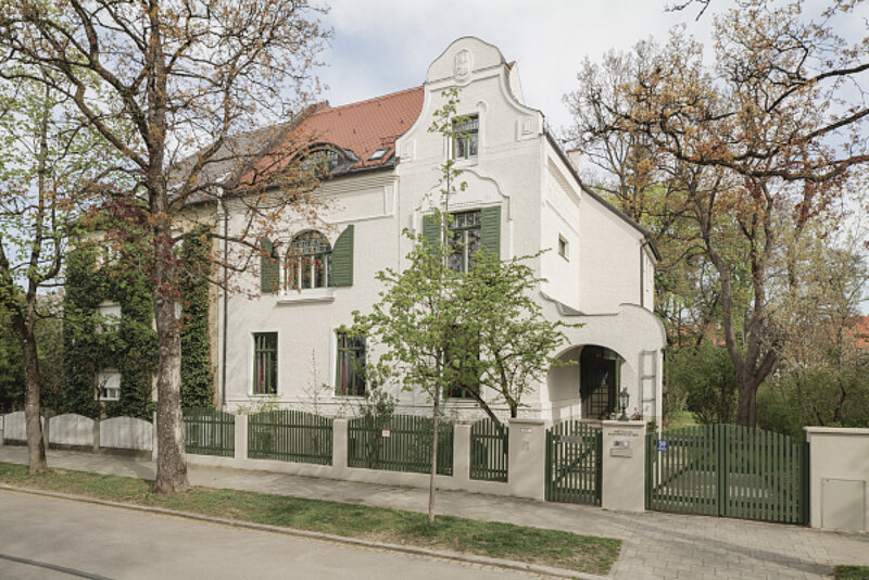 Weißes Haus mit grünen Fensterläden und grünem Zaun unter Bäumen